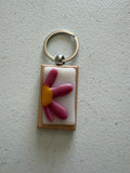 Pink daisy fused glass keychain with elongated petals and small yellow center on white glass tile with wood backing and silver key ring