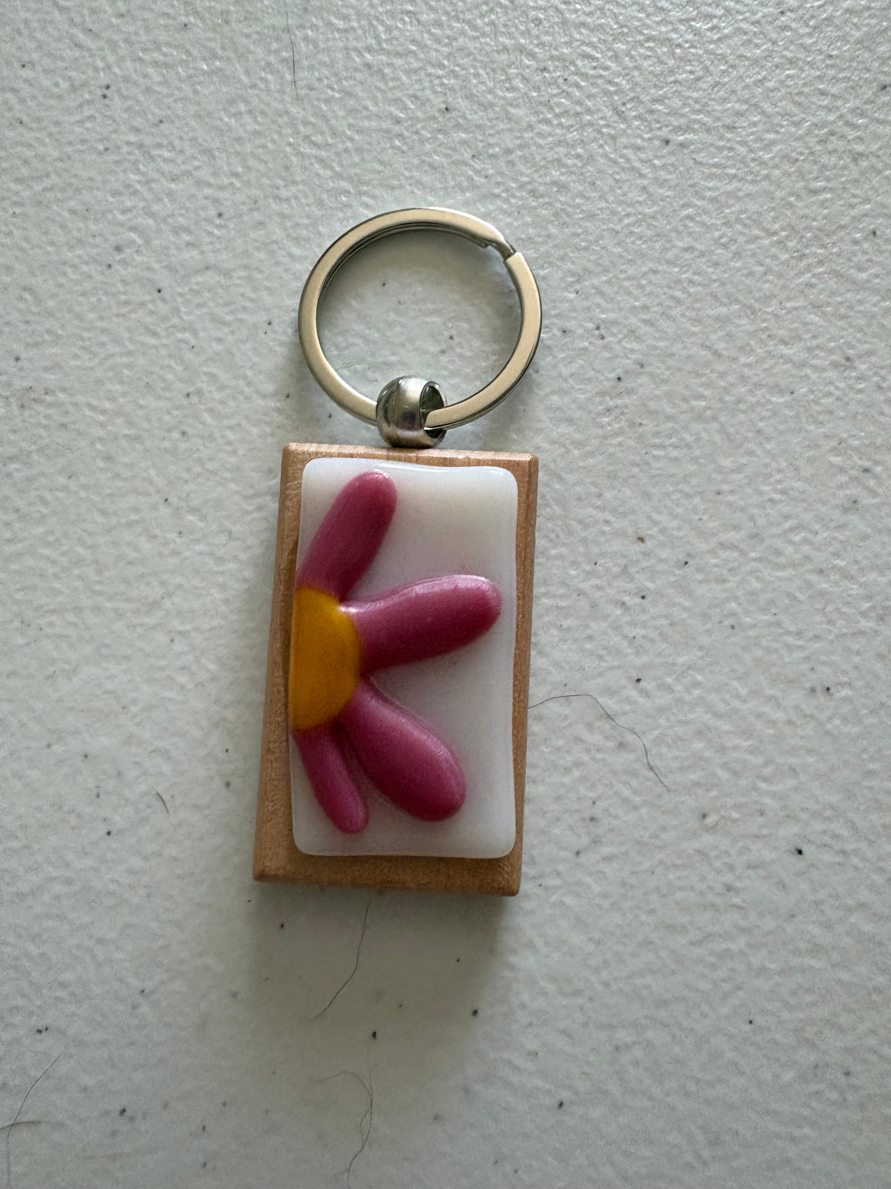 Pink daisy fused glass keychain with elongated petals and small yellow center on white glass tile with wood backing and silver key ring