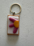 Pink rounded flower fused glass keychain with large yellow center on white glass tile with wood backing and silver key ring