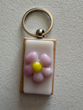 Pink daisy fused glass keychain with yellow center, set in a natural wood frame with silver key ring