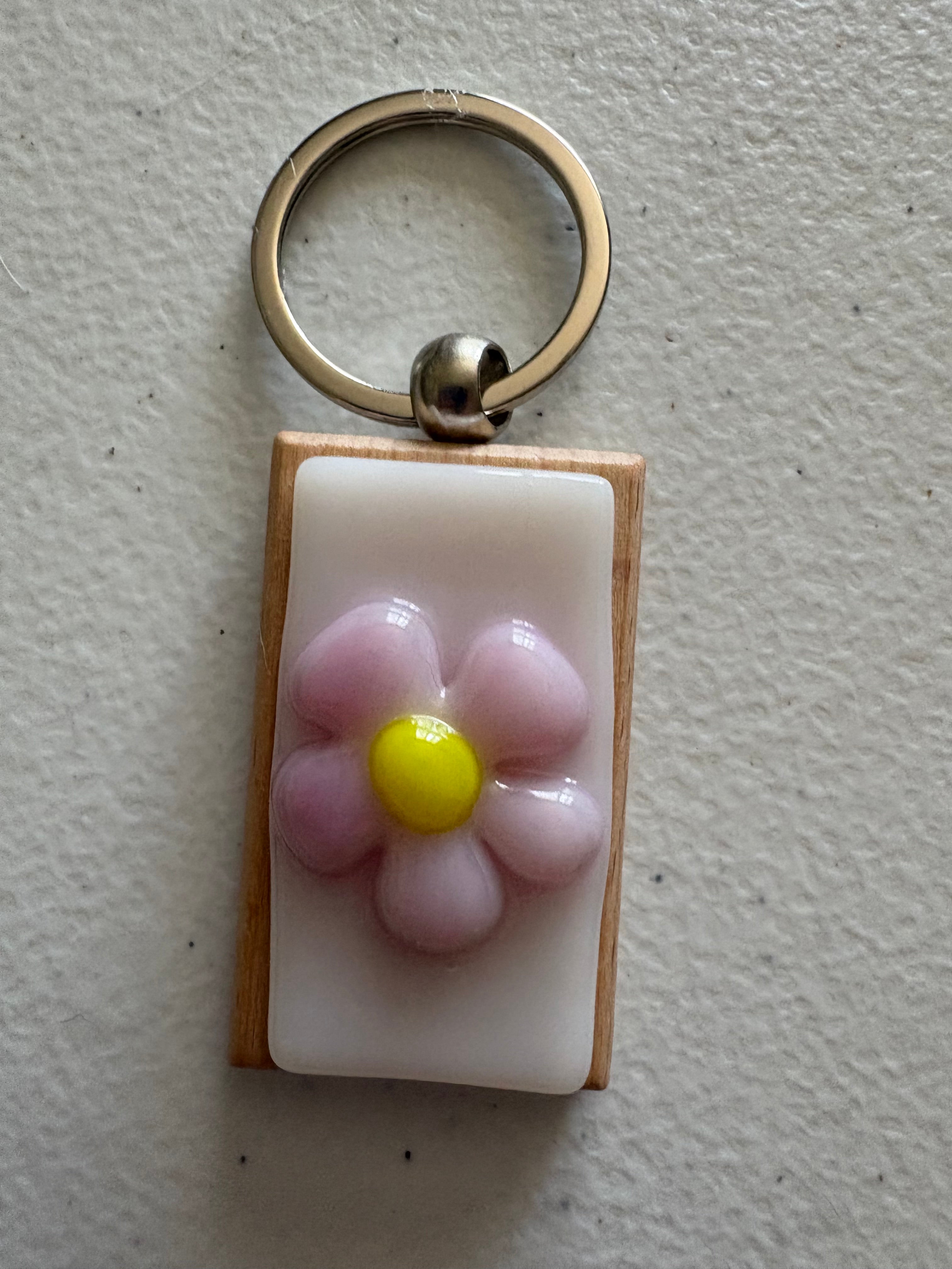 Pink daisy fused glass keychain with yellow center, set in a natural wood frame with silver key ring
