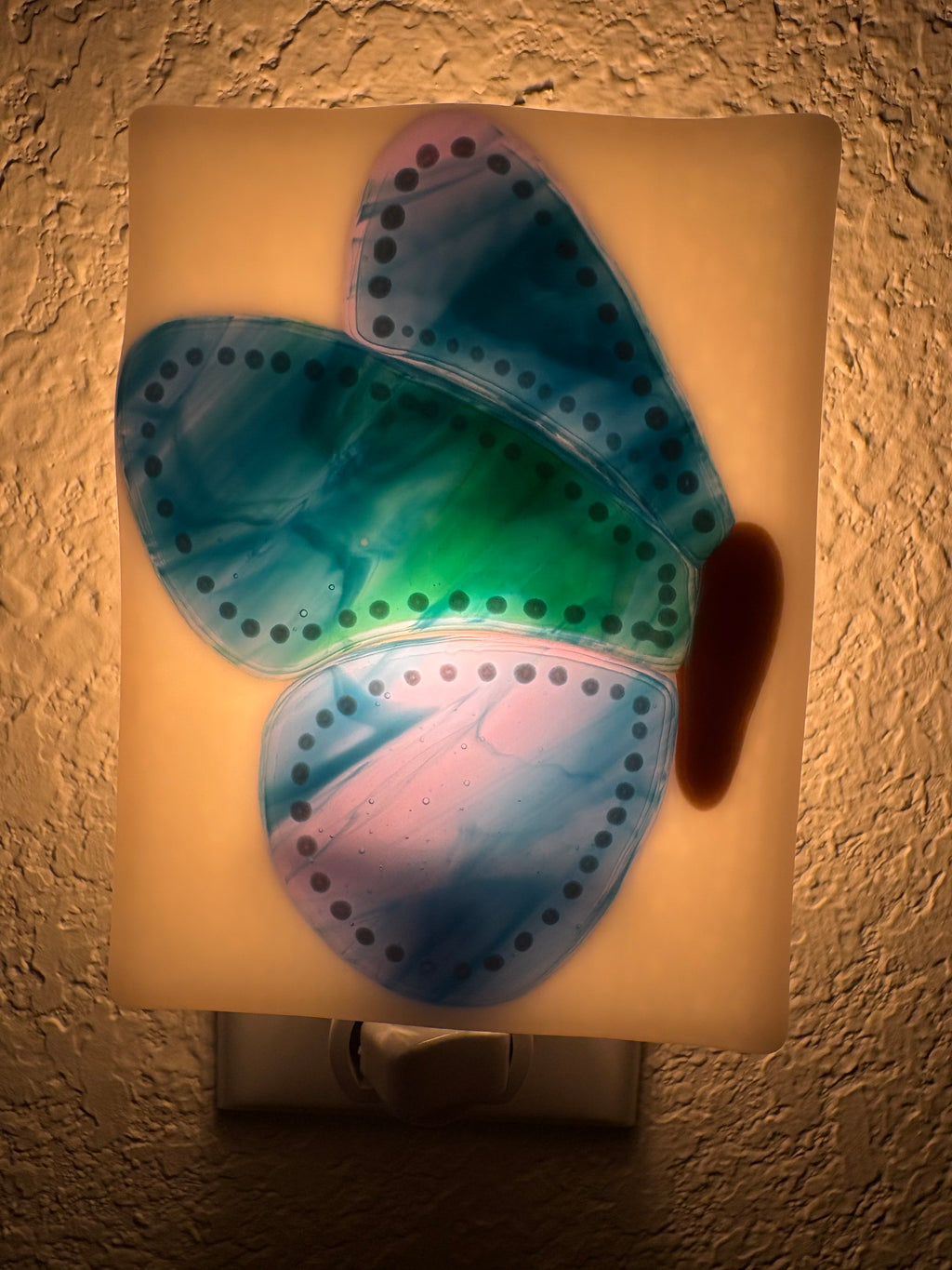 Blue and green fused glass butterfly nightlight unlit, showing white background with cobalt blue and green wings outlined in white dots
