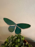 Emerald green and teal iridescent stained glass butterfly plant stake displayed in a leafy planter