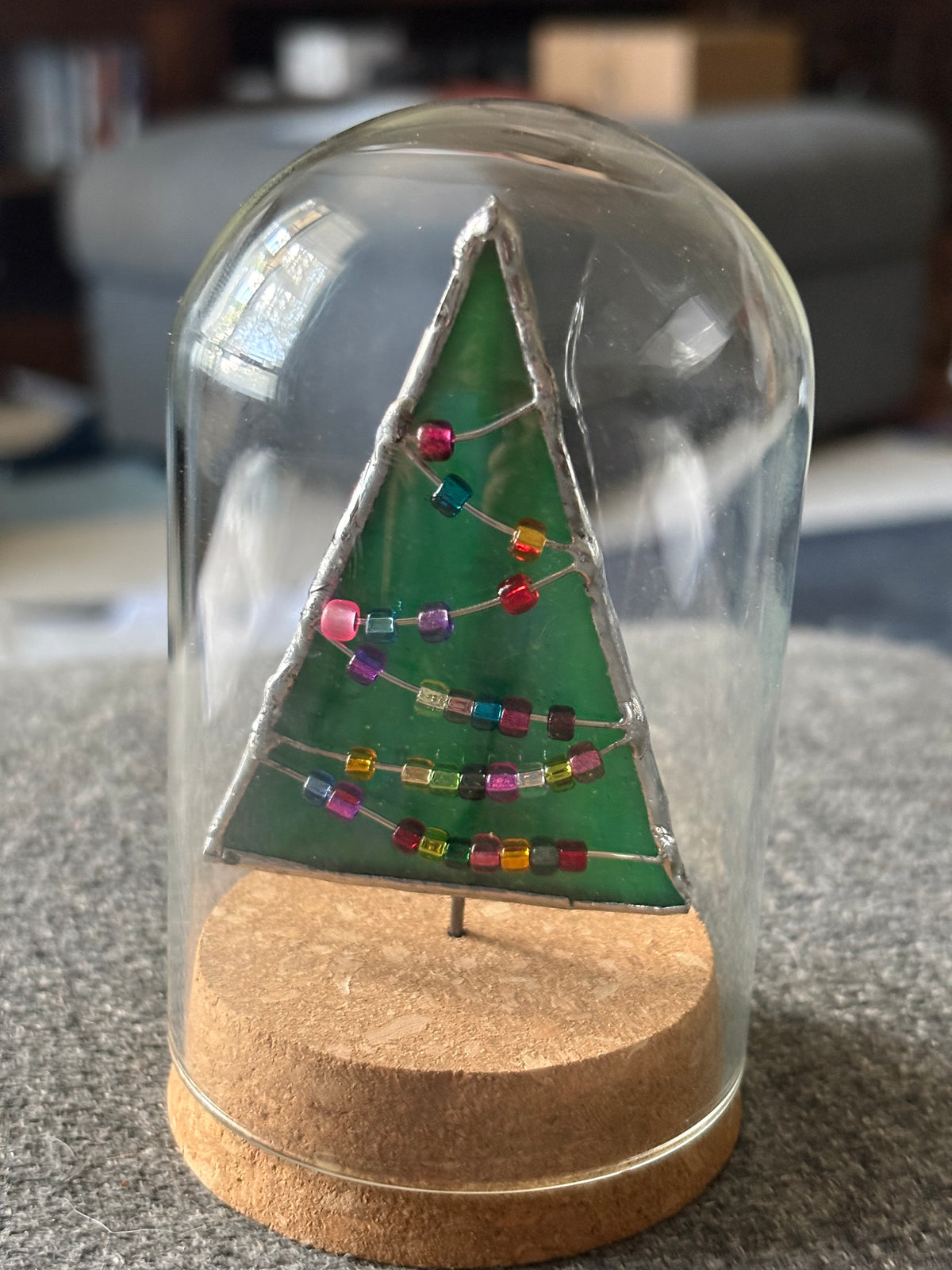 Close-up of a green fused-glass Christmas tree with colorful bead garlands and a wooden base