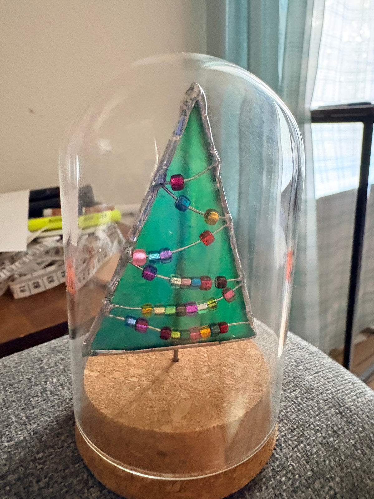 Handmade green fused-glass Christmas tree decorated with colorful bead garlands on a wooden display base